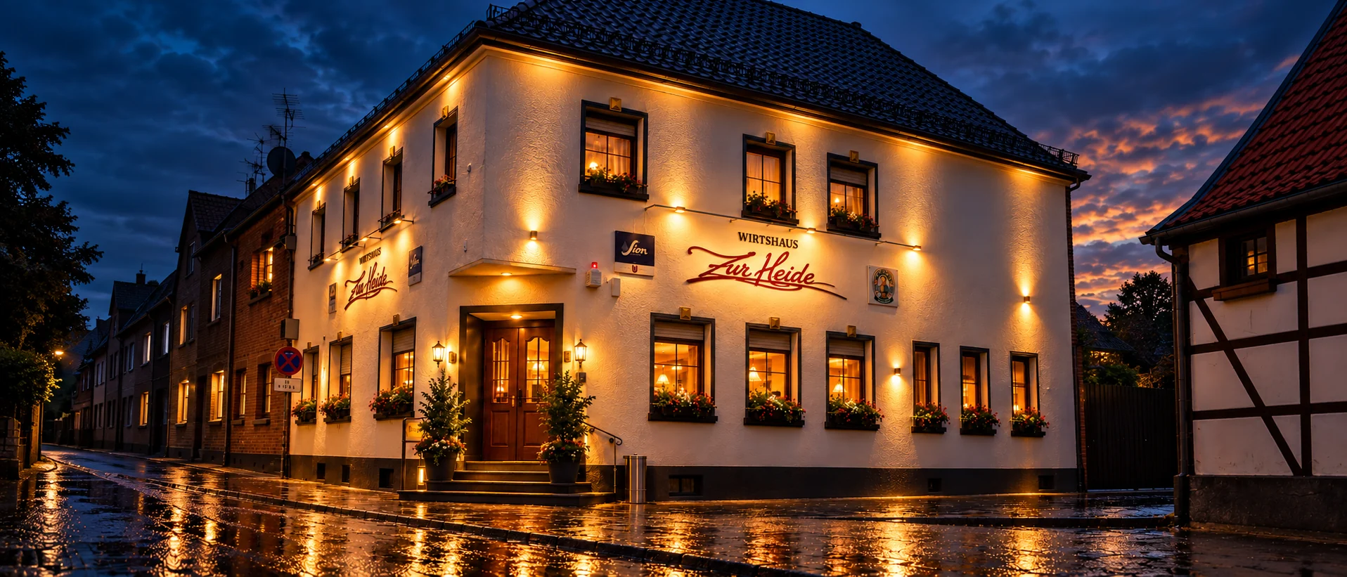 Das Wirtshaus Zur Heide am Abend nach dem Regen, die nasse Straße spiegelt das warme Licht der Fassade